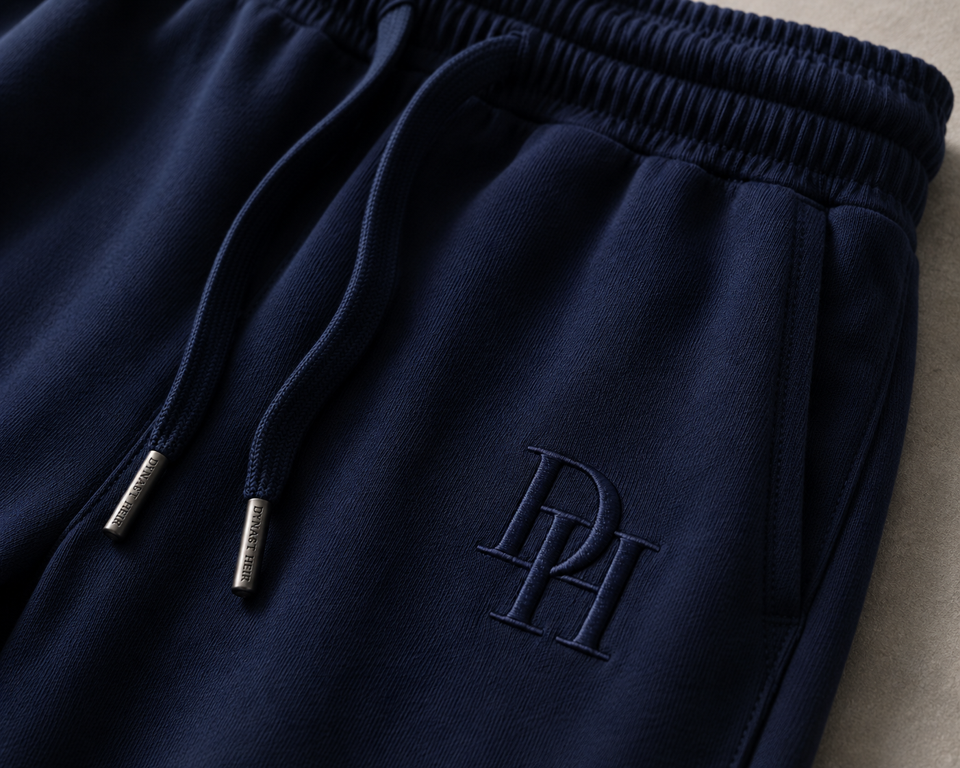 Close-up of the DH monogram and tipped drawcords on the navy Foundation Sweatpant