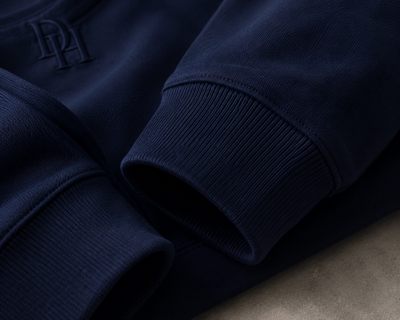 Close-up of deep navy Dynast Heir fabric, ribbed cuffs, and tonal DH monogram